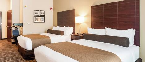 A hotel room with two beds, a nightstand, a lamp, and framed pictures on the wall.
