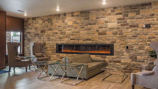 A modern living room with a stone wall, a fireplace, leather sofas, and glass coffee tables. - Cobblestone Inn & Suites - Ashland (Ashland)