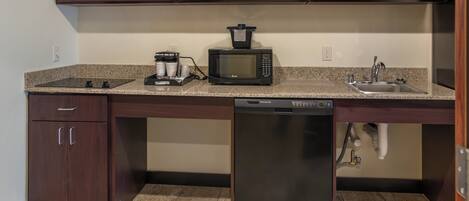 A kitchen with dark wooden cabinets, a granite countertop, a microwave, a coffee maker, a dishwasher, and a sink.