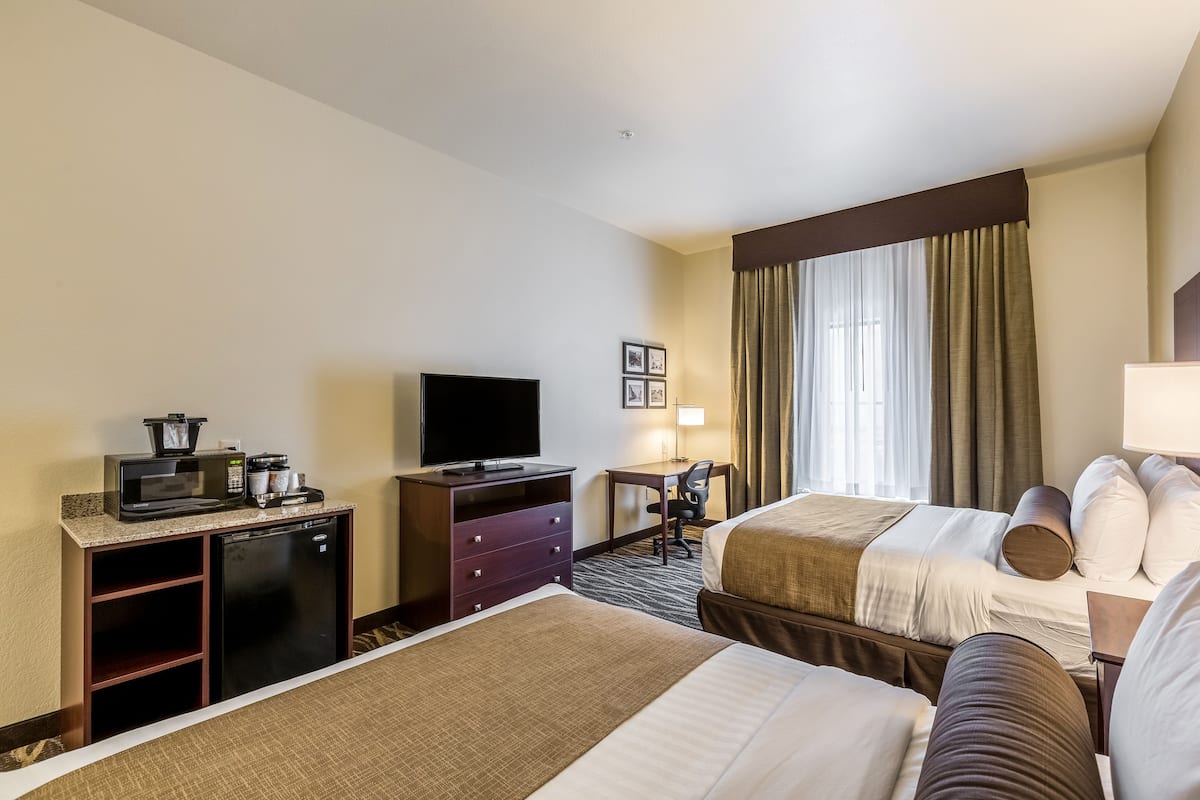 A hotel room with two beds, a desk with a TV, a minibar, and a window with curtains.