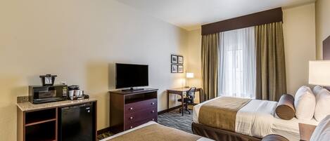Una habitación de hotel con dos camas, un escritorio con computadora, televisor y minibar.