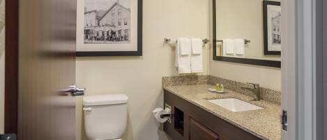 A bathroom with a toilet, sink, and mirror. There are framed pictures on the wall.