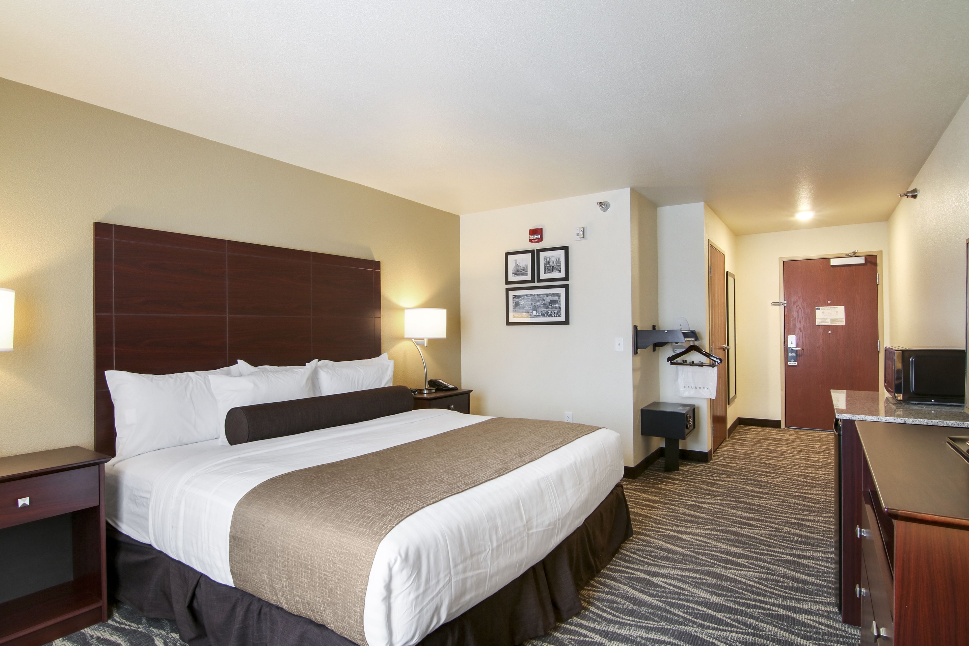 Una habitación de hotel con una cama grande, mesitas de noche, un escritorio con una silla, un microondas y un perchero.