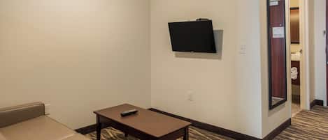 A hotel room with a bed, a small table with a remote control, a wall-mounted TV, and a mirror.