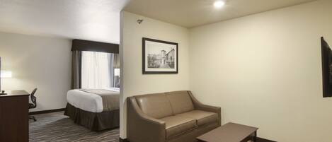 A hotel room with a bed, a sofa, a small table, and a desk.