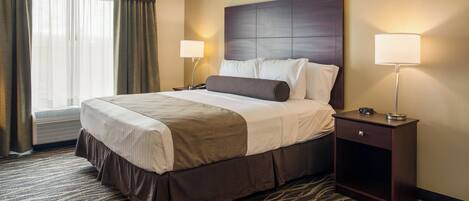 A hotel room with a large bed, two bedside tables, a window with curtains, and a patterned carpet.