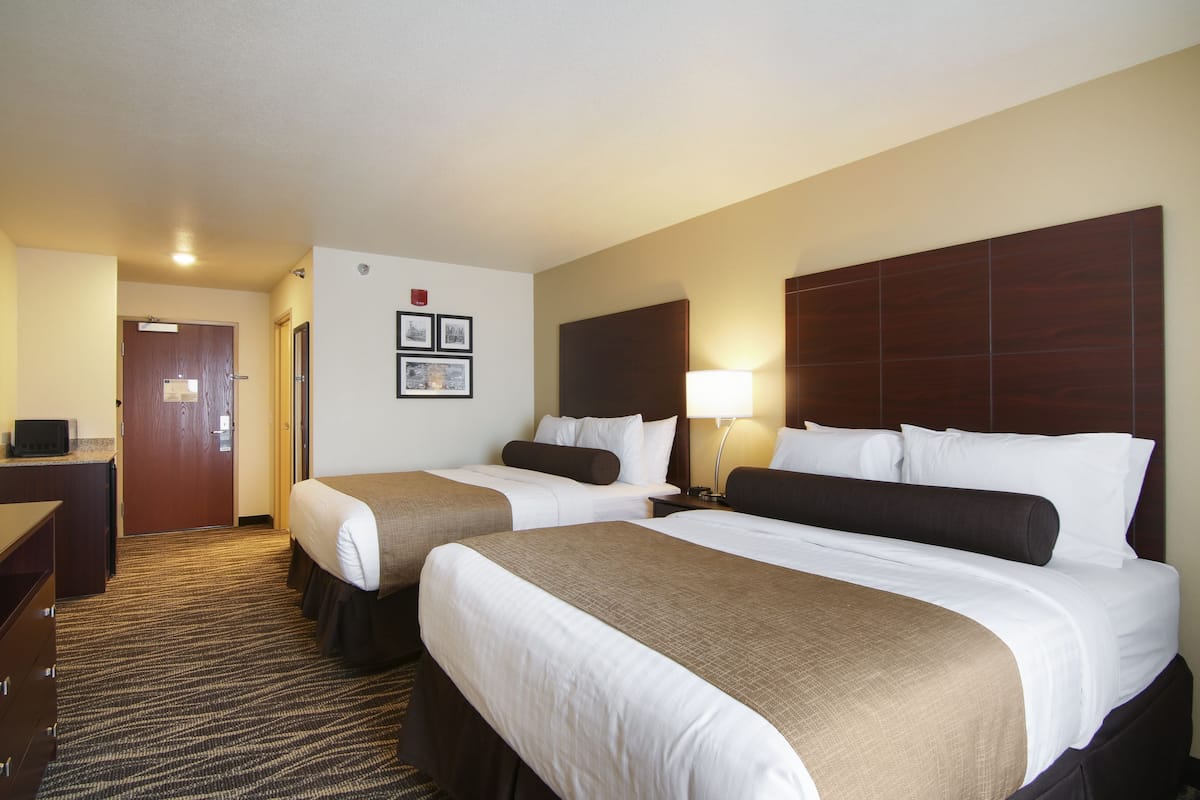 A hotel room with two beds, a desk, a lamp, and a door.