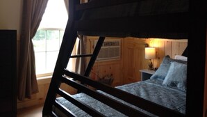 Una cama individual en literas en una habitación con ventana, paredes de madera y una mesita de noche con lámpara.