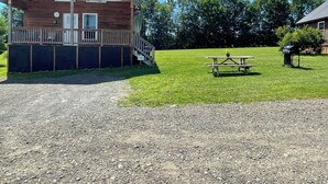 Una cabaña rústica con terraza de madera y una mesa de picnic en una zona con césped.