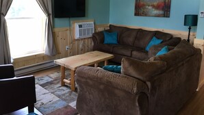Una sala de estar acogedora con un sofá marrón, una mesa de centro de madera y un televisor montado en la pared.