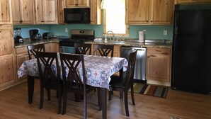 Una cocina con armarios de madera, microondas, estufa, lavaplatos y una mesa de comedor con sillas.