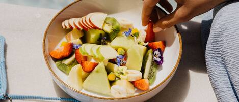 A bowl of fruit salad with a variety of fruits including apples, oranges, and kiwi, placed on a table near a pool.