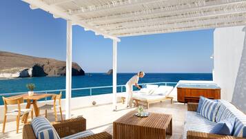 Un espace extérieur aménagé, abrité et doté de mobilier en osier, d’une table en bois, et offrant une vue sur la mer et les falaises.