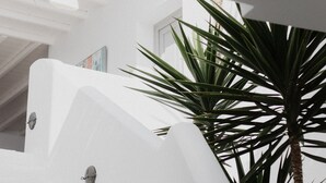 A white architectural structure with a geometric design, a palm tree, and a door with a glass panel. - Melian Boutique Hotel & Spa (Milos)