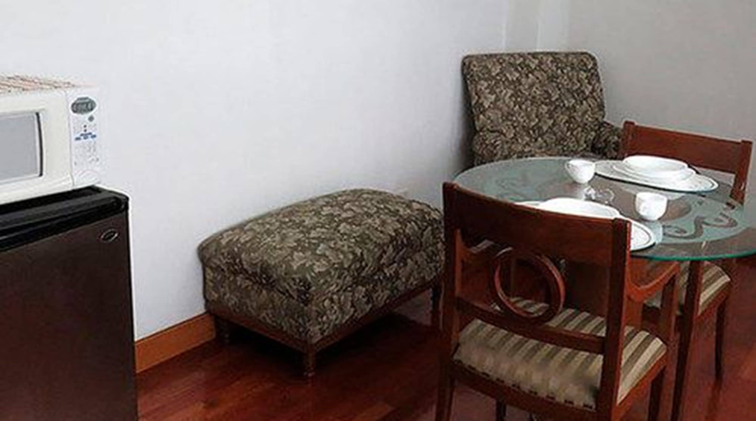 Une cuisine compacte équipée d’un four à micro-ondes, d’un petit réfrigérateur, d’une table de salle à manger ronde avec des chaises et d’un pouf à motifs.