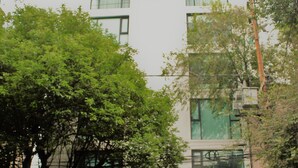 Un edificio de varios pisos con un acceso de garaje, un árbol en la entrada y un coche estacionado.