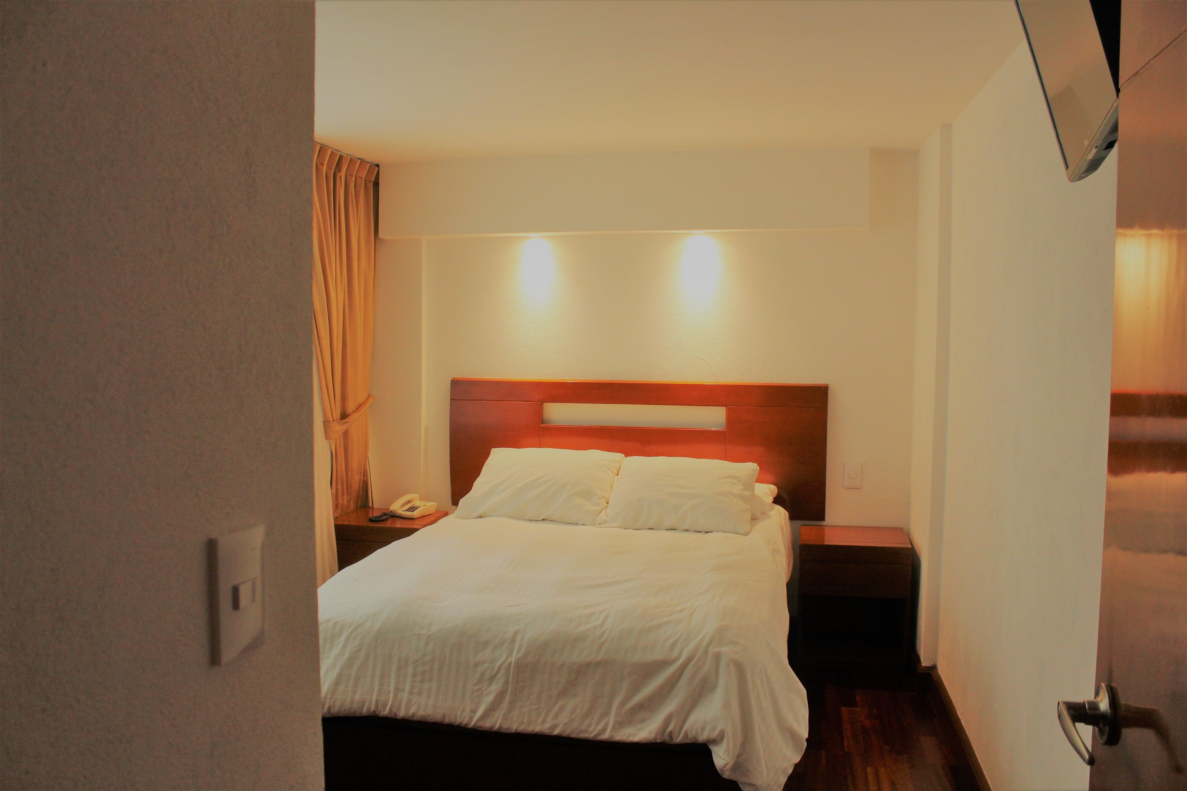 A hotel room with a bed, bedside table, and a nightstand with a lamp.