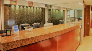 Zona de recepción de un hotel con mostrador de mármol, un cartel de bienvenida y un área de descanso con sillones.