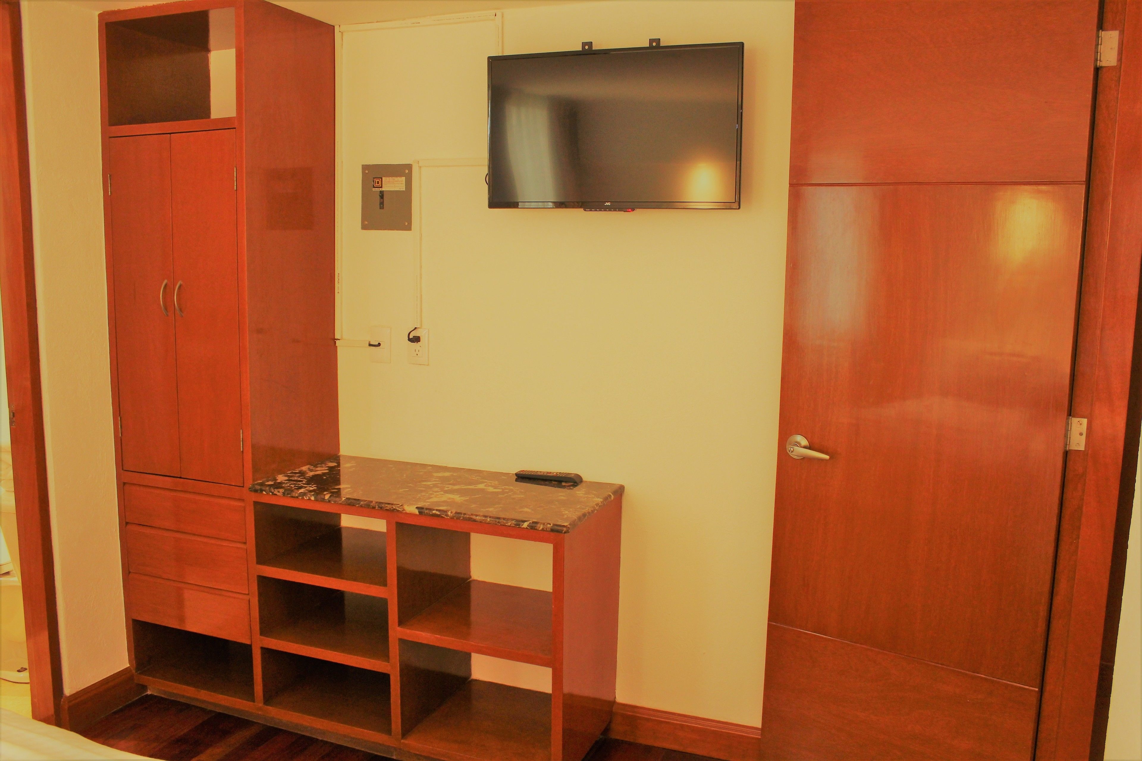 Ein Zimmer mit einem Holzschrank, einem kleinen Holztisch und einem darüber befestigten Fernseher sowie einer Tür.