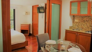 Habitación de hotel con cama, una mesita con platos y tazas, televisor montado en la pared y armarios de madera.