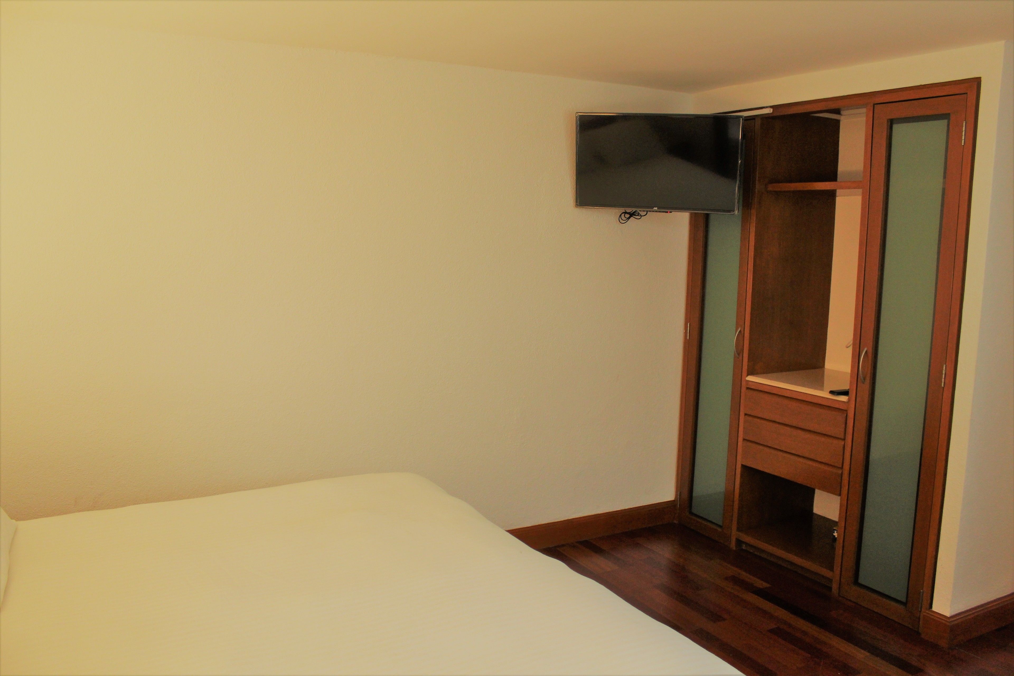 A bedroom with a bed, a wardrobe with a mirror, and a television mounted on the wall.