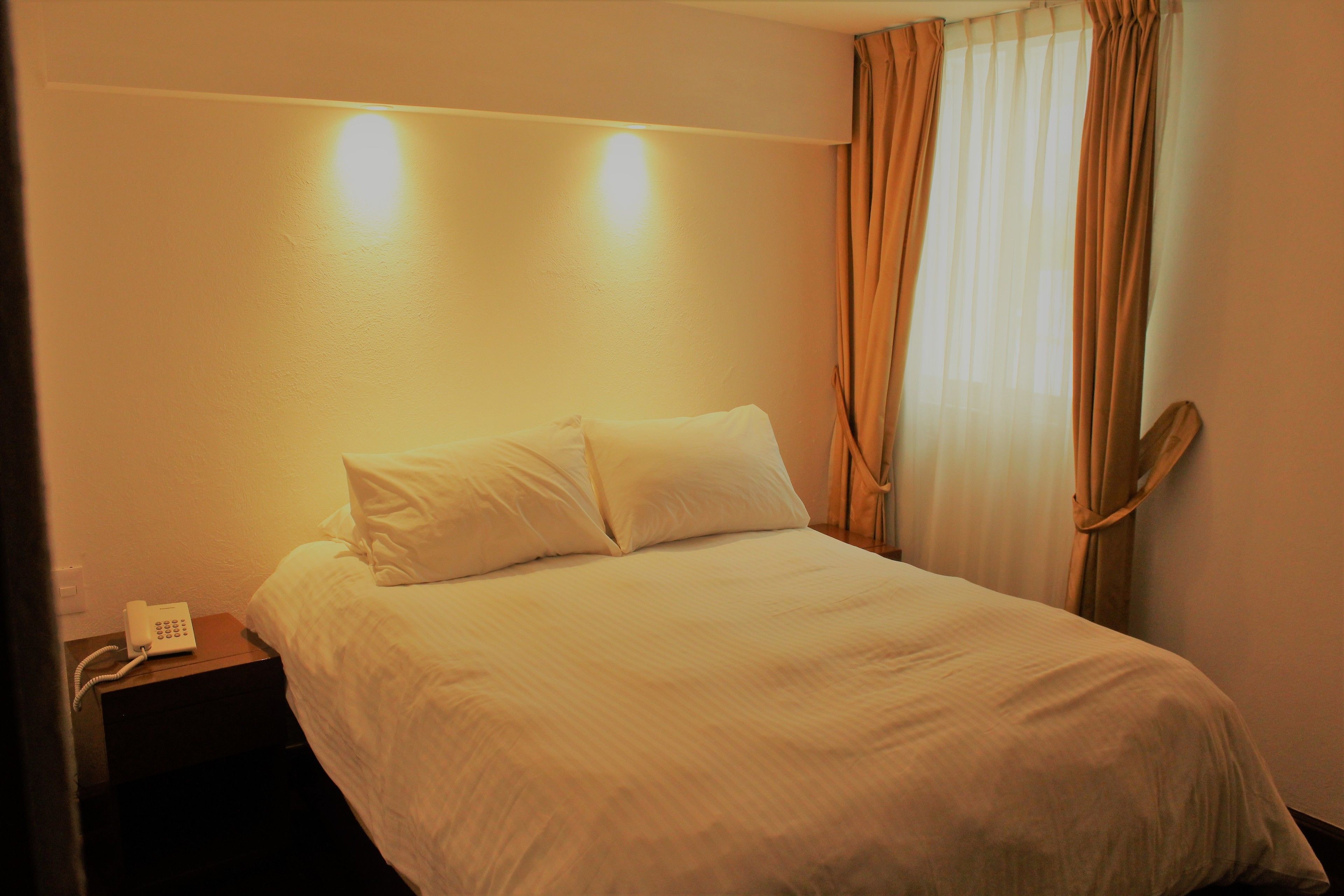 Une chambre d’hôtel avec un lit, une table de chevet avec un téléphone et des rideaux.
