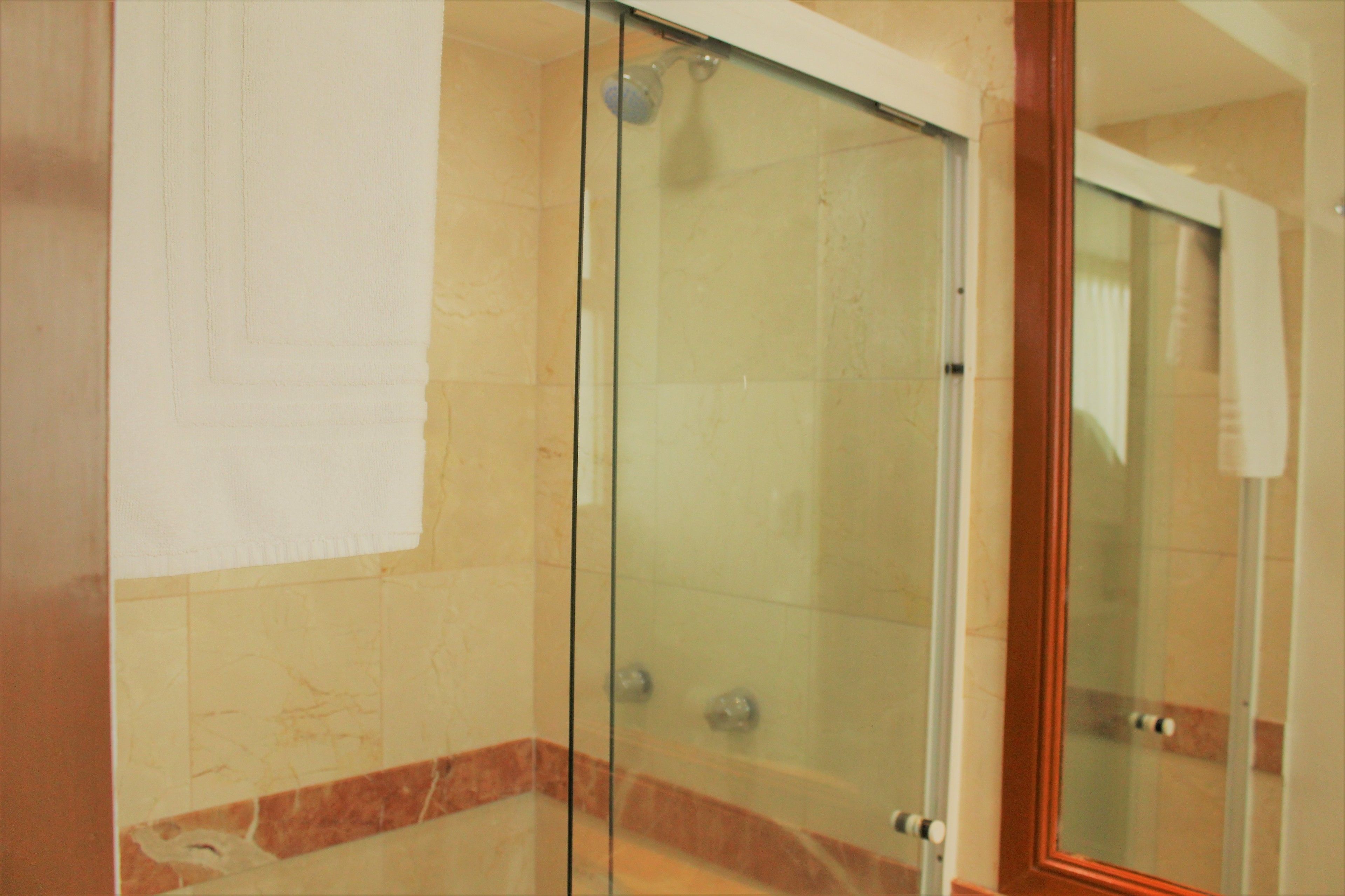 A glass-enclosed shower with a marble-tiled wall and a wooden frame.