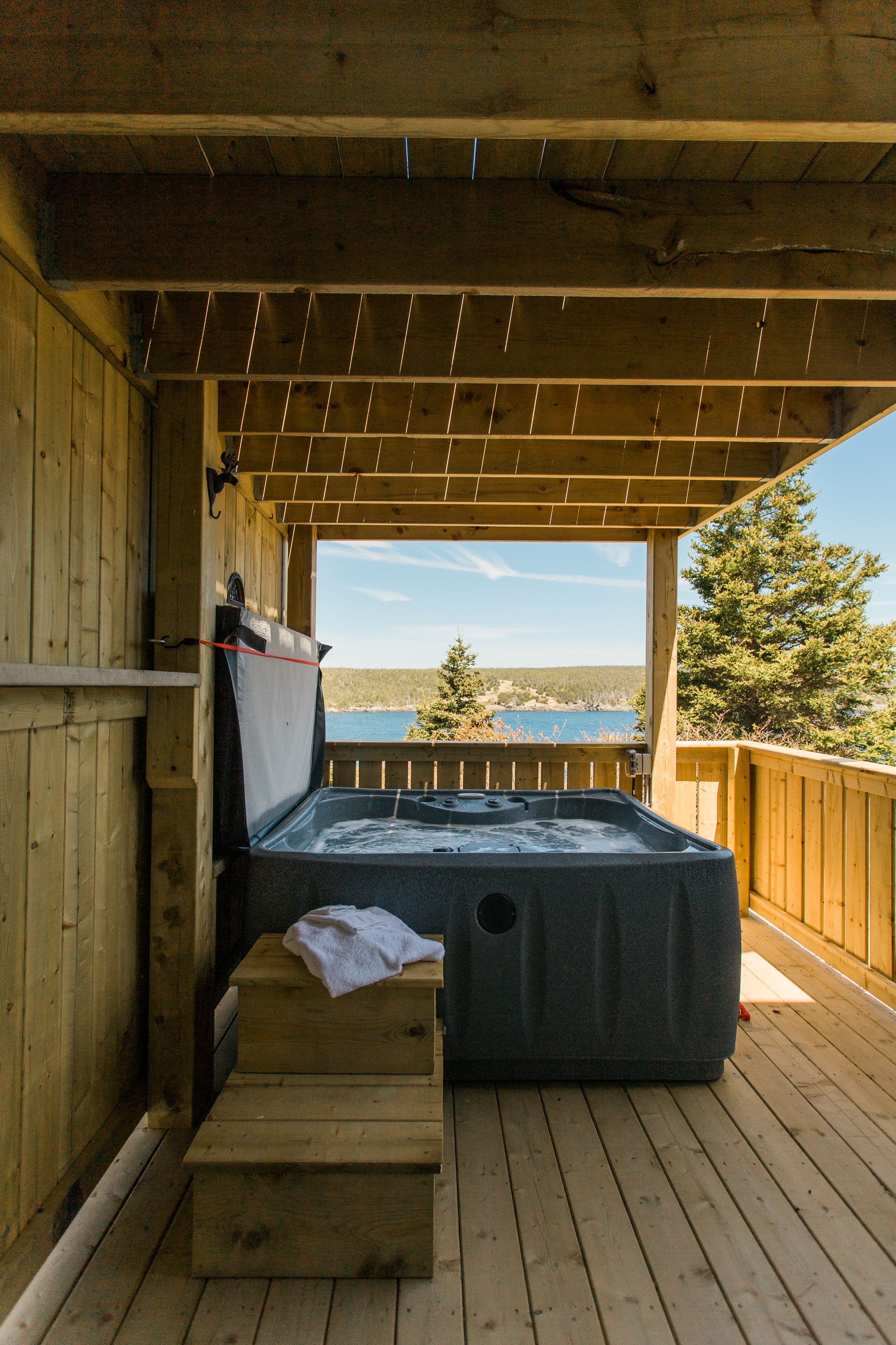 Una terraza de madera con un jacuzzi, paredes de madera y vista al agua.