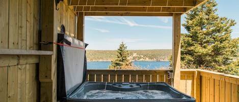Una terraza de madera con un jacuzzi, paredes de madera y vista al agua.