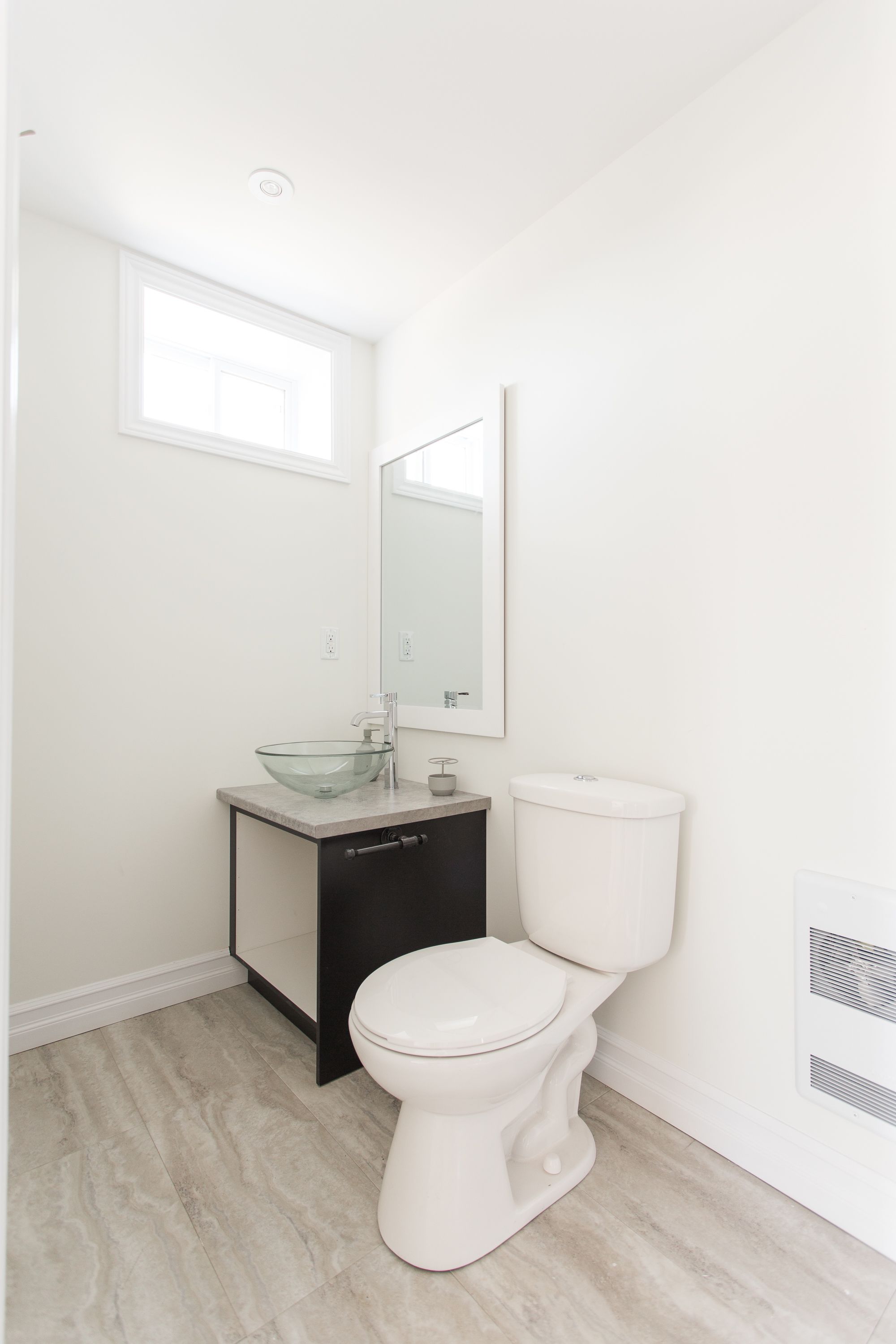 Une salle de bain moderne avec un lavabo en verre, des toilettes blanches et un grand miroir.