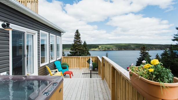A wooden deck with a hot tub, outdoor seating, and a view of a lake. - Whale House Guest House (Mobile)