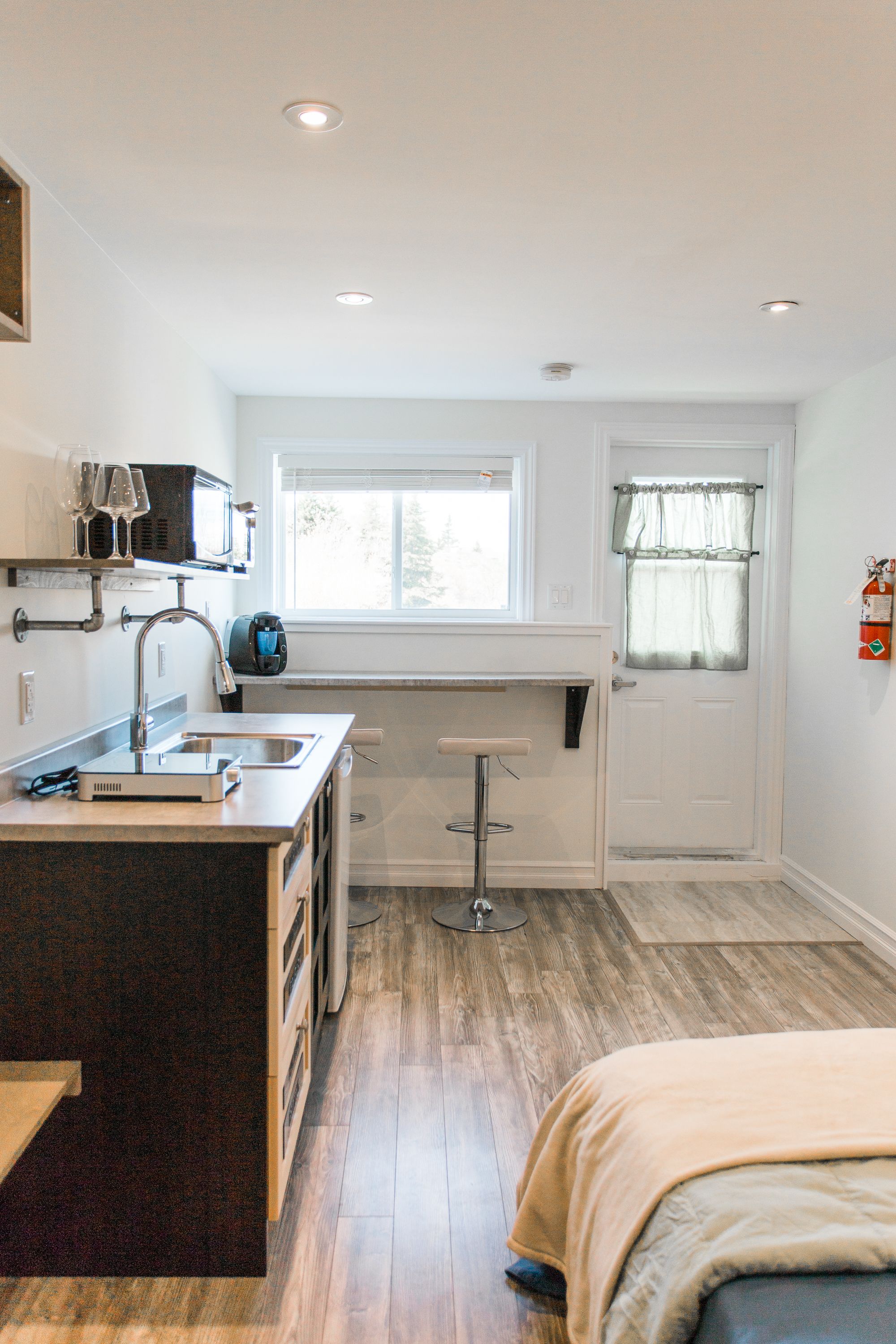 A compact kitchen with a built-in island, a window with curtains, and a door with a fire extinguisher.