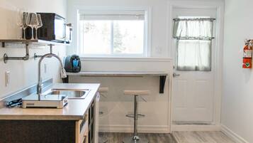 A compact kitchen with a built-in island, a window with curtains, and a door with a fire extinguisher.