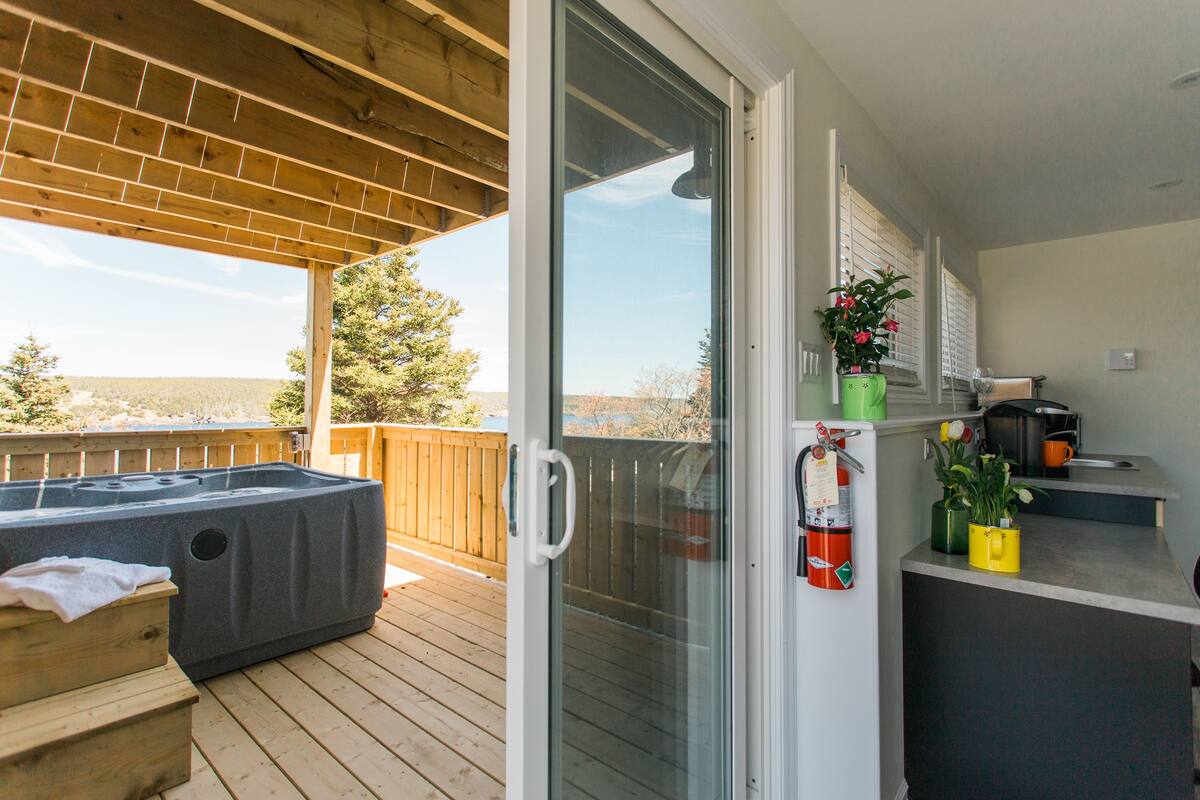 A balcony with a hot tub, a sliding glass door, and a small kitchen area with a coffee maker and a plant.