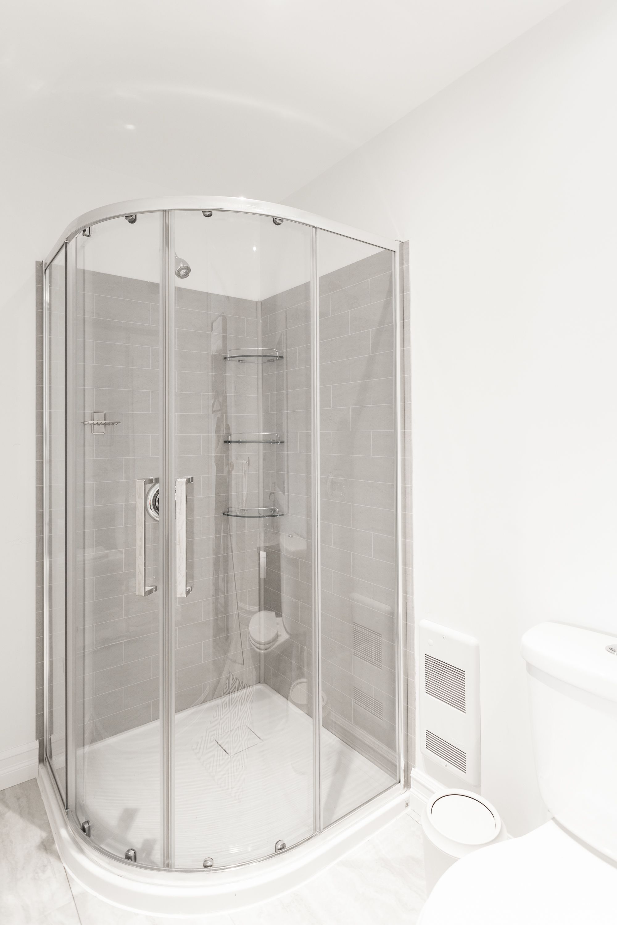 Een moderne badkamer met een douche met glazen wand, een toilet en ventilatie.