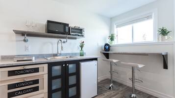 A modern kitchen with a built-in microwave, a refrigerator, and a sink. There are bar stools and a window with plants on the windowsill.