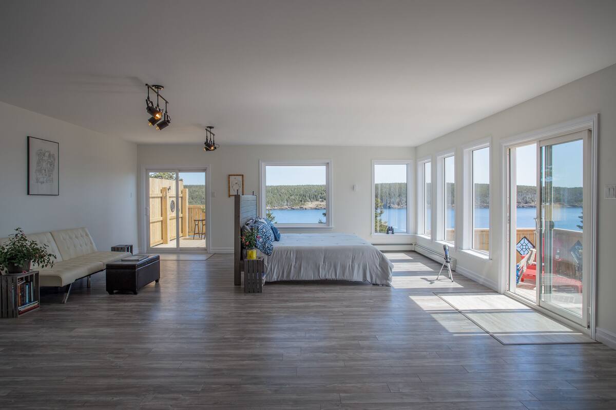 A spacious bedroom with a large bed, a sofa, and a view of a lake.