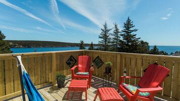 A wooden deck with red Adirondack chairs, a hammock, and potted plants.