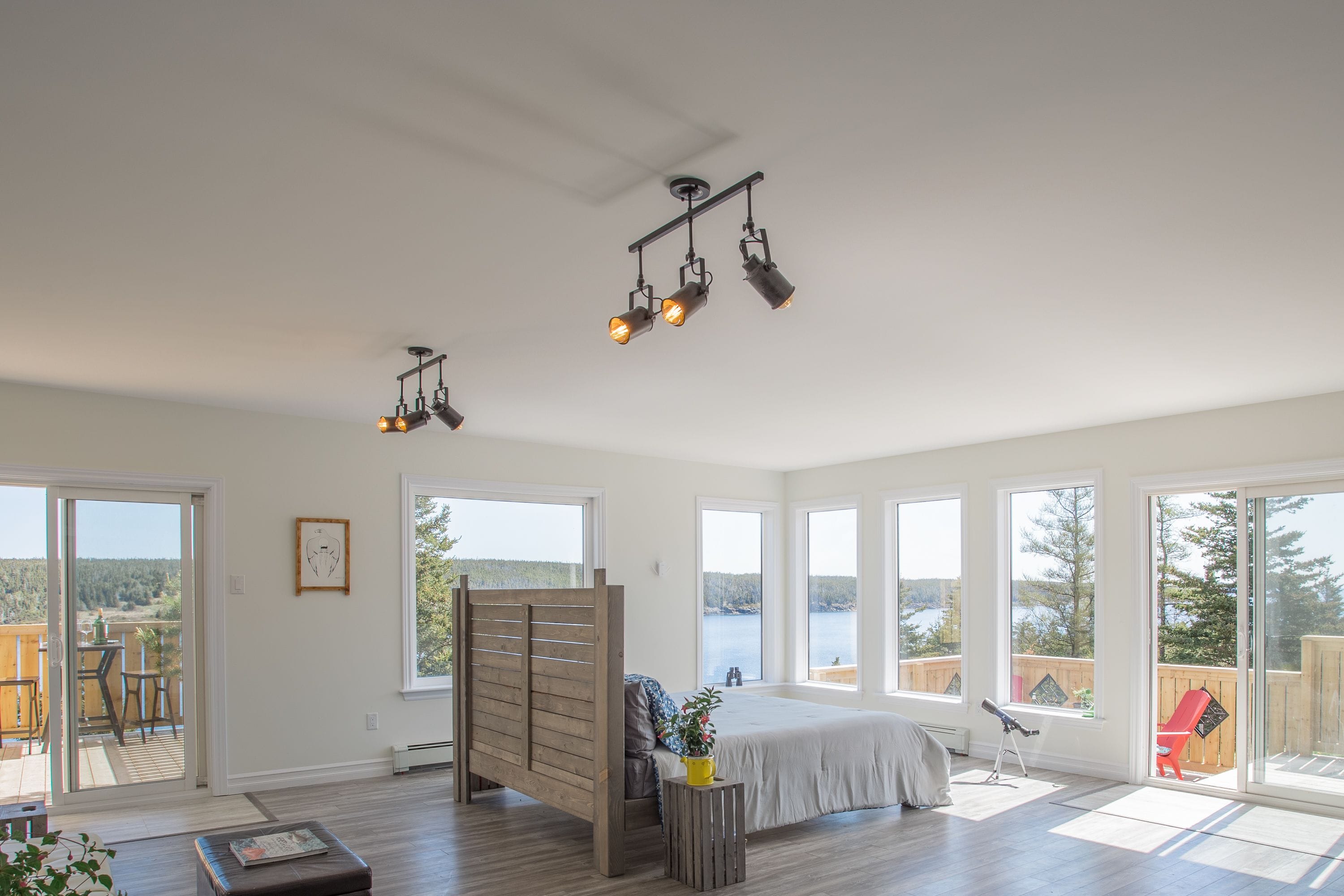 Un dormitorio amplio con una cama grande, un cabecero de madera y vistas a un lago a través de amplias ventanas.