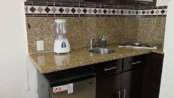 A compact kitchen with a microwave, blender, sink, and dark cabinets.