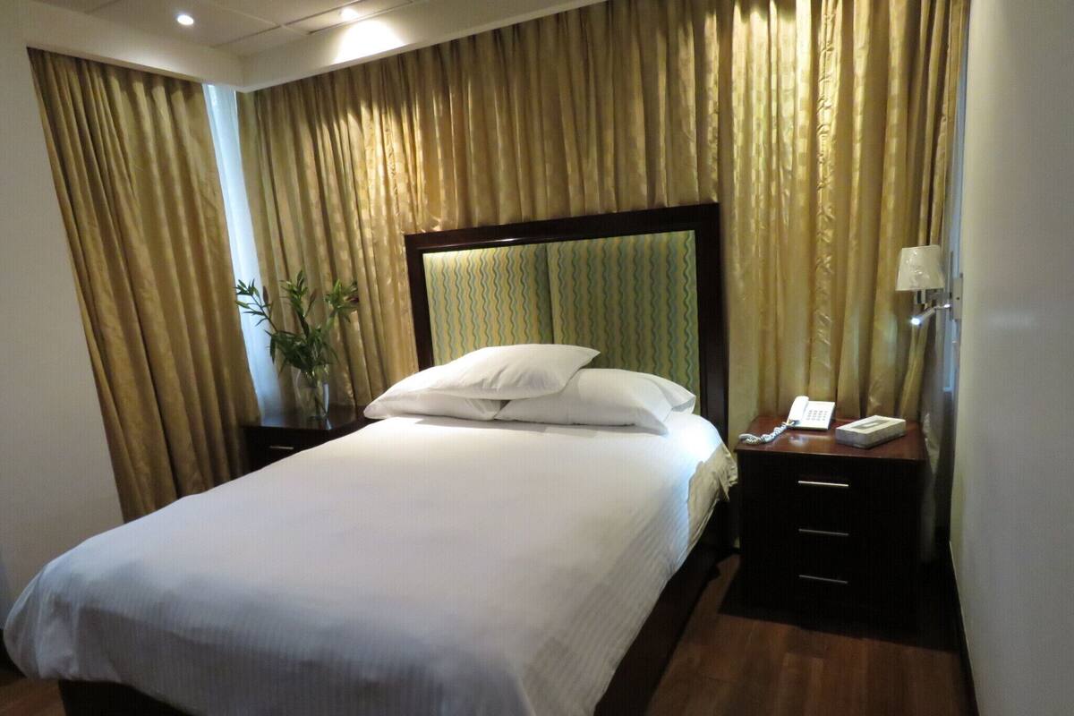 Una habitación de hotel con una cama grande, una mesita de noche con lámpara y cortinas.