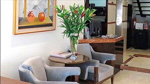 A reception area with a round table, two grey chairs, a potted plant, and a framed picture of apples on the wall.