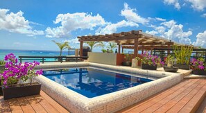 A pool area with a wooden deck, a pergola, and potted plants.