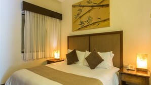 A hotel room with a large bed, two bedside tables with lamps, a window with curtains, and a wall art piece.