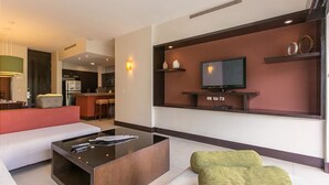 A modern living room with a sofa, a coffee table, a TV mounted on a wall, and a kitchen area in the background. - Aldea Thai 27 by Tripintravel (Playa del Carmen)