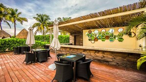 An outdoor patio with wooden flooring, black wicker furniture, and a thatched roof. - Elements GH01 by Tripintravel (Playa del Carmen)