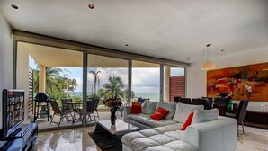A spacious living room with a large white sofa, a coffee table, and a view of the ocean. - Elements 123 by Tripintravel (Playa del Carmen)