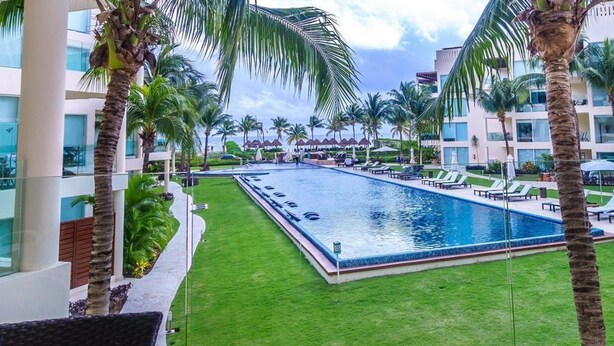 A swimming pool surrounded by palm trees and a modern building with a glass facade. - Elements PH19 by Tripintravel (Playa del Carmen)