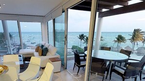Een moderne woonkamer met een glazen wand met uitzicht op de oceaan, ingericht met een bank, stoelen en een eettafel.
