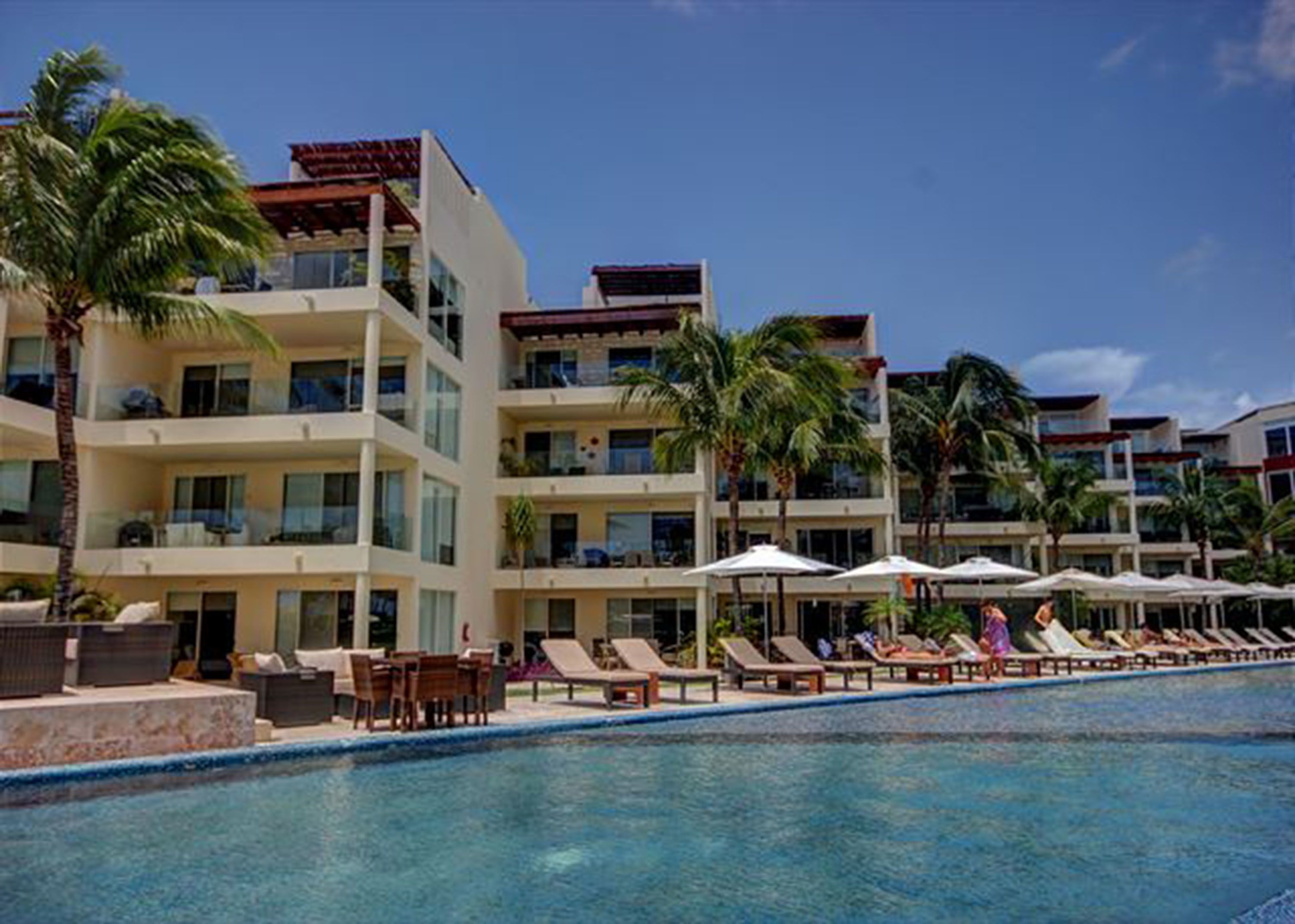 A hotel with a pool area, multiple balconies, and palm trees.